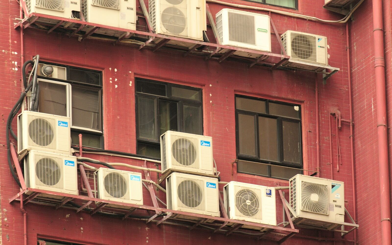 Many air conditioning units from different brands on the side of a building