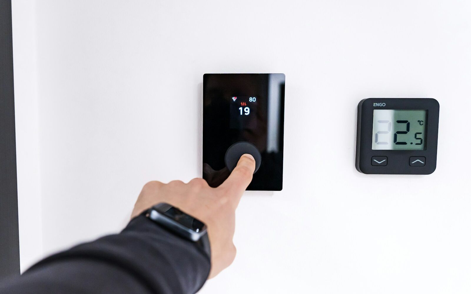 A hand adjusting a wall-mounted digital thermostat